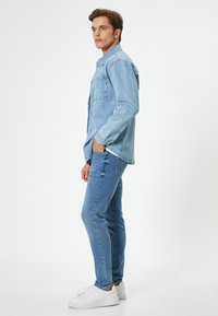 Chaqueta de mezclilla azul claro con frente abotonado y bolsillo en el pecho, combinada con jeans azul claro a juego y zapatillas blancas.