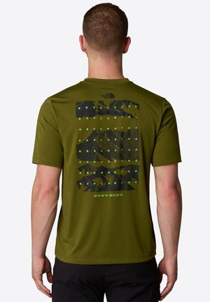 Mężczyzna noszący oliwkowo-zieloną koszulkę The North Face z czarną górską grafiką i powtarzającym się napisem „Never Stop Exploring” na plecach.