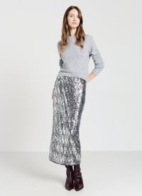 Grauer gestrickter Pullover, langer silberner Paillettenrock und bordeauxfarbene Absatzstiefel. Das Outfit besticht durch einen strukturierten, schimmernden Effekt der Pailletten.