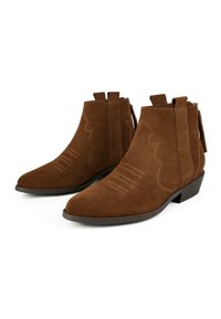 Stivali ankle in suede marrone presentano una punta appuntita, tacco basso a ragno, cuciture decorative e anelli laterali alla caviglia per un facile indossamento.