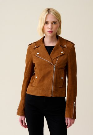 Veste de moto en daim marron avec des zips argentés, des boutons-pression et des épaulettes. Présente un design ajusté et des manches longues.