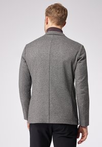 Gray textured blazer with a herringbone pattern, tailored fit, and a dark collar. Visible seams and sleek, straight-cut sleeves.