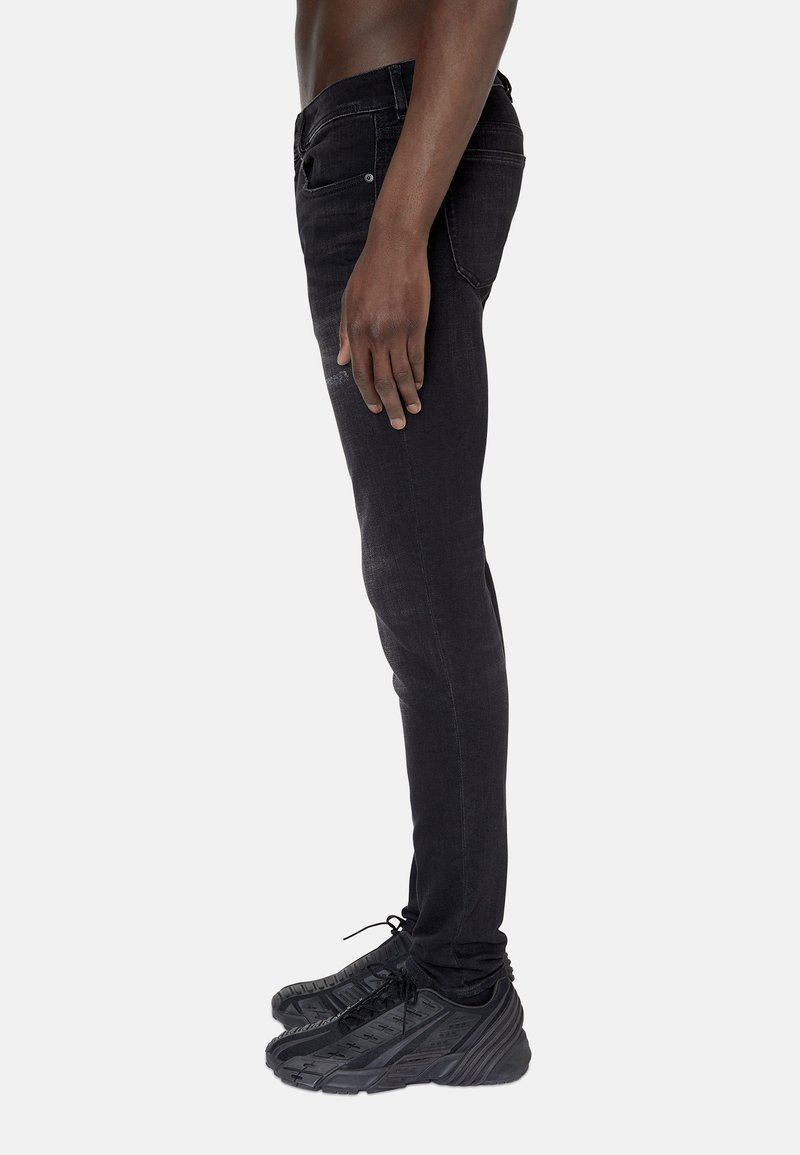 Jean noir slim en denim avec une texture lisse, doté d'une poche avant et porté avec des chaussures de sport noires.
