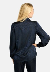 Tumši zila satīna blūze ar smalku čūskas rakstu, garām piedurknēm, apkakli un brīvu piegriezumu ar izliekta stila apakšu.