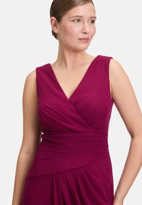 Sukňa bez rukávov v hlbokom magentovom odtieni s výstrihom do V, zhodeným telom a splývajúcou sukňou, vyrobená z hladkej a plynulej tkaniny.