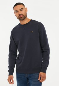 Granatowa bluza crewneck z teksturowanej tkaniny, z małym złotym logo na piersi i ribbowymi ściągaczami, oferująca dopasowany krój.