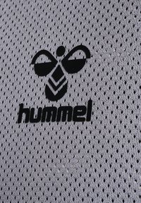 Il tessuto a rete grigia presenta un evidente logo Hummel nero e una grafica di un'ape, caratterizzato da piccole perforazioni su tutta la superficie.