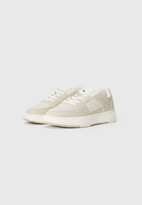 Beige athletic shoes with a textured upper, white accents, round toe, and flat sole. Includes lace-up front and padded collar.