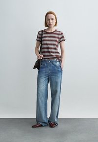 Ριγέ καφέ και λευκό T-shirt συνδυασμένο με ανοιχτό μπλε jeans φαρδιάς γραμμής με ρίγες στο πλάι, που ολοκληρώνεται με μπορντό παπούτσια και τσάντα ώμου.