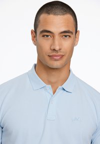 Polo shirt azzurro realizzato in un tessuto traspirante. Presenta un colletto classico, una patta con tre bottoni e un logo ricamato sul petto.