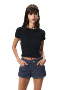 Čierny rebrovaný crop top s krátkymi rukávmi, skombinovaný s džínsovými šortkami s vysokým pásom. Má okrúhly výstrih a priliehavý strih.