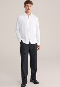 Biela košeľa s dlhým rukávom a gombíkmi, šedé prispôsobené nohavice, čierne topánky. Hladká tkanina, klasický golier, uvoľnený strih, viditeľné dva bočné vrecká.