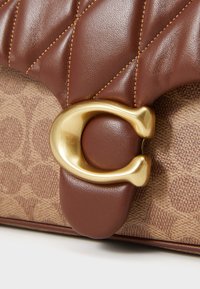 Borsa in pelle marrone con texture trapuntata, accessori in oro e base in tela a motivi. Presenta un evidente dettagli di chiusura circolare.