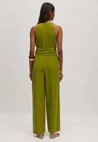 Grüner ärmelloser Jumpsuit mit tailliertem Bund, weitem Bein und Reißverschluss auf der Rückseite. Glattes Material mit strukturierter Oberfläche.