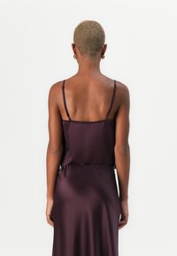 Lilla satiin Kleid õhukeste rihmadega, millel on vormitud rind ja voogav seelik, mis ulatub taljest allapoole, esitledes minimalistlikku disaini.