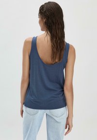 Navyblauwe mouwloze tanktop met een lage rugontwerp, gemaakt van zachte stof, in combinatie met lichtblauwe spijkerbroek.