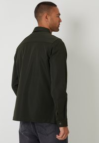 Donkergroene shirt met een kraag en knoopmanchetten, gemaakt van gladde stof; heeft een rugpas en een getailleerde pasvorm.