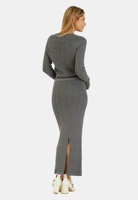 Grau gestreiftes Strickkleid mit vertikalen Streifen, verziert mit kleinen Edelsteinen und mit einem Schlitz hinten. Kombiniert mit weißen Blockabsatzschuhen.