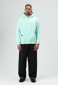 Lichtgroene hoodie met voorvak en witte branding, gecombineerd met zwarte wijduitlopende spijkerbroek en zwarte veterboots.