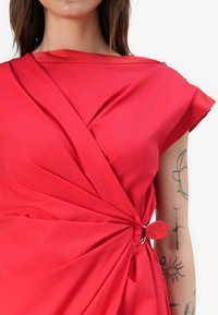 Rotes Kleid aus glattem Stoff, mit einem drapierten Design, verknotetem Detail und silberner Ringbeschlägen an der Schulter.