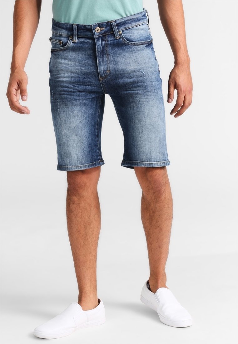 Shorts en denim bleu clair avec finition délavée, design à cinq poches, ourlets retroussés et coupe décontractée, accompagnés de chaussures blanches sans lacets.