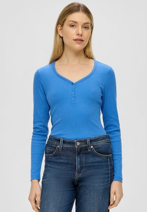 Langarm, ribbelgetextureerd top in felblauw, met een V-hals en een drieknoopssluiting. Gecombineerd met hoge taille donkere blauwe jeans.