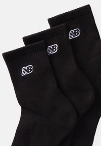 Trei perechi de șosete negre din bumbac texturat. Fiecare șosetă are un logo alb brodat New Balance aproape de vârf.