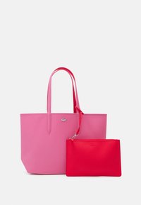 Sac cabas rose au design élégant, comprenant une pochette rouge texturée. Les deux ont des poignées lisses assorties et un logo argenté.