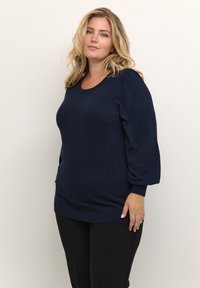 Námořnická modrá pletená svetr s kulatým výstřihem, nabíranými rukávy a žebrovaným lemem. Hladká textura a přiléhavý střih.