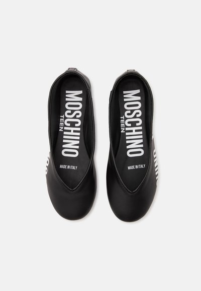 Paire de chaussures Moschino Teen noires type slip-on avec logo blanc et inscription "Made in Italy" à l'intérieur, présentée sur fond blanc uni.