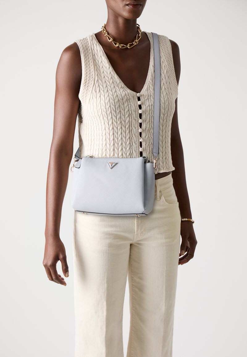 Sac bandoulière bleu clair avec surface texturée, quincaillerie en argent et détail de logo. Porté avec un haut en tricot crème et un pantalon large beige.