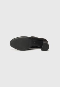 Black suede ankle boots with a textured rubber sole and a slight heel. The bottom features ridged patterns for enhanced grip.