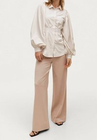 Ljust rosa blus med ballongsärmar, knäppning och rynkade detaljer, i kombination med beige vida byxor och svarta sandaler med remmar.