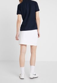 Women's outfit featuring a navy polo shirt and a white skirt. The look includes white socks and gray Nike sneakers.