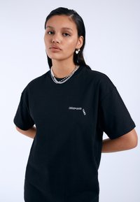 Camiseta de algodón negra con un corte relajado, que presenta el texto "DREAM GOOD TIMES" en blanco en el pecho. Textura suave y mangas cortas.