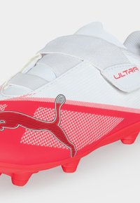 Λευκό και κόκκινο ποδοσφαιρικό παπούτσι Puma με κλείσιμο με λουράκι, υφασμένο σχέδιο και μαύρο λογότυπο Puma στο πλάι.