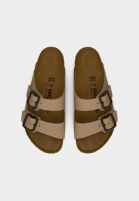 Μπεζ σανδάλια ανοιχτού τύπου με δύο ρυθμιζόμενες μαύρες αγκράφες σε κάθε ένα, καφέ εσωτερικές σόλες και σημάδια μεγέθους 41 εσωτερικά.