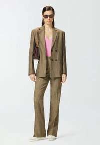 Blazer doppiopetto marrone e pantaloni coordinati, indossati su un top rosa a coste. Gli accessori includono occhiali da sole e una piccola borsa.