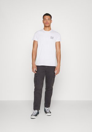 White short-sleeve t-shirt with small black text design, paired with dark gray cargo pants featuring side pockets and black sneakers.