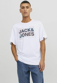 Witte katoen t-shirt met een grafische print van "JACK & JONES" in zwart en rood, ontspannen pasvorm en korte mouwen. Blauwe denim spijkerbroek zichtbaar.
