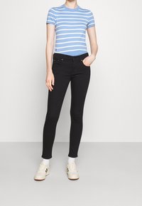 Blå och vitrandig t-shirt med rund hals, matchad med svarta skinny jeans. Vita sneakers med en diskret design som fulländar outfiten.