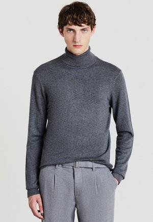 Maglione grigio a collo alto in tessuto morbido con maniche lunghe. Presenta un design aderente e una texture sottile, abbinato a pantaloni grigi chiari.
