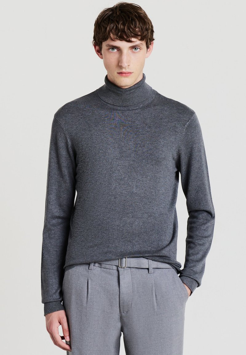 Grauer Rollkragenpullover aus weichem Material mit langen Ärmeln. Er zeichnet sich durch ein tailliertes Design und eine subtile Textur aus, kombiniert mit hellgrauen Hosen.
