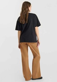 Top negro de manga corta con un patrón de puntos blancos, combinado con pantalones anchos marrones. La tela parece suave y tiene un corte relajado.