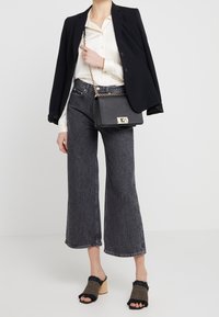 Blazer nero sopra una camicia button-down color crema, abbinato a jeans a gamba larga grigio scuro a vita alta e mule aperte nere a righe. Borsa a tracolla in argento.