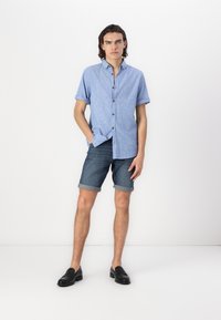 Chemise à manches courtes bleu clair, avec un motif texturé, associée à un short en denim foncé à revers et des mocassins noirs.