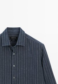 Donkerblauw hemd met lange mouwen en witte verticale krijtstrepen, knoopsluiting aan de voorkant, en puntige kraag, met label Massimo Dutti, gemaakt van 100% linnen.