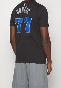 Czarna bawełniana koszulka T-shirt z napisem "DONČIĆ" w szarym kolorze nad niebieskim, perforowanym "77" z tyłu, z małym logo NBA na karku.