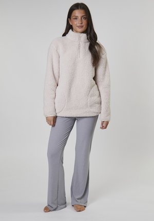 Lichtroze fleece pullover met hoge kraag en rits aan de voorkant, gecombineerd met grijze flared broeken. Textuurstof en zijzakken zijn zichtbaar.