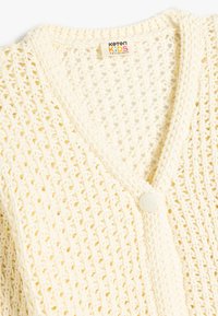 Lätt, krämfärgad stickad cardigan med V-ringning, som har ett strukturerat öppet väv och en enda knäppning framtill.